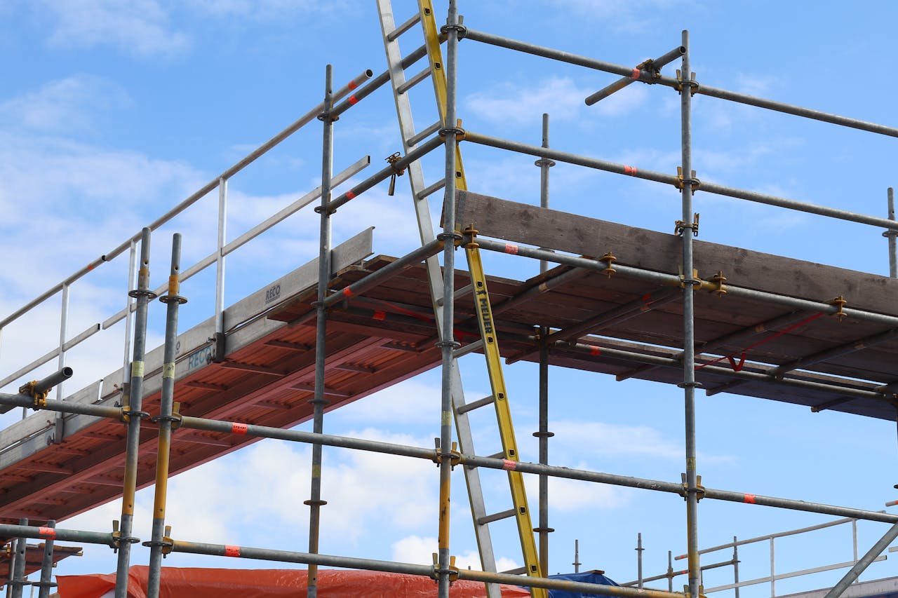 heros-img Detailed view of a construction site scaffolding structure and ladder against a bright blue sky.